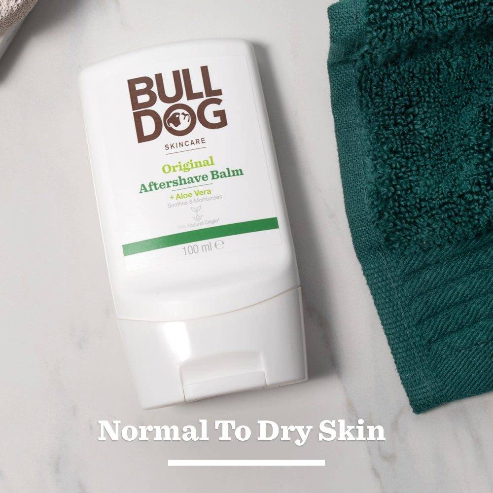 A bottle of Original After Shave Balm made with natural origin ingredients rests on a white surface beside a green towel, with Normal To Dry Skin text below.