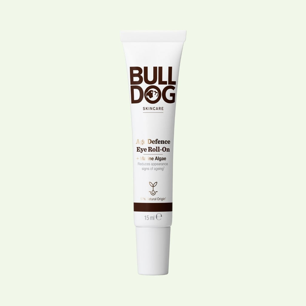 A tube of Age Defence Eye Roll-On for mens skincare, featuring marine algae to reduce signs of aging, stands upright on a light background. The white packaging displays brown and gold text.