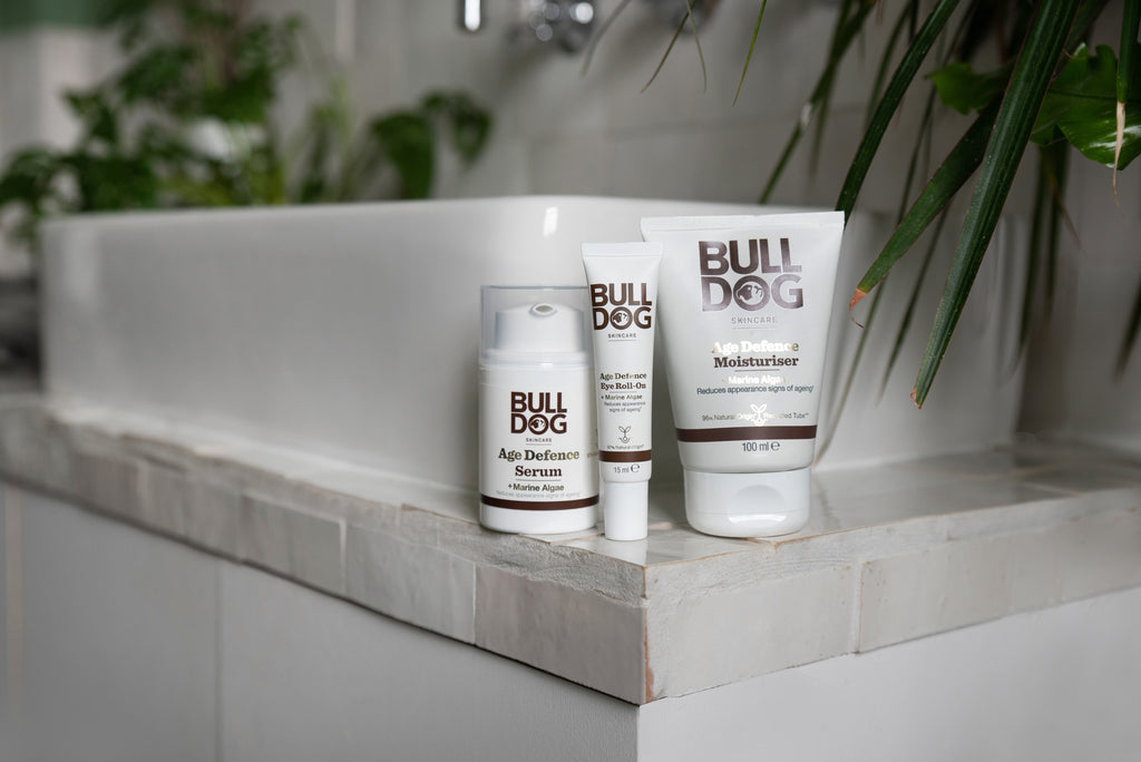 The Age Defence Skincare Routine Bundle sits on the edge of a white bathroom sink, surrounded by green plants.