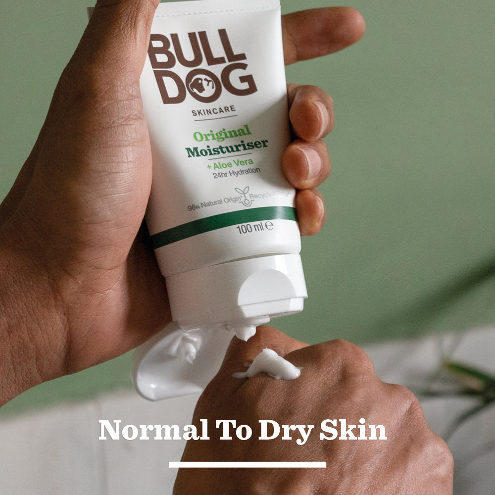 A person sprays Bulldog Skincare Original Spray Deodorant Bundle, featuring Natural-Origin Ingredients. Normal To Dry Skin is displayed, while a soft green background sets a fresh tone for your grooming regimen.