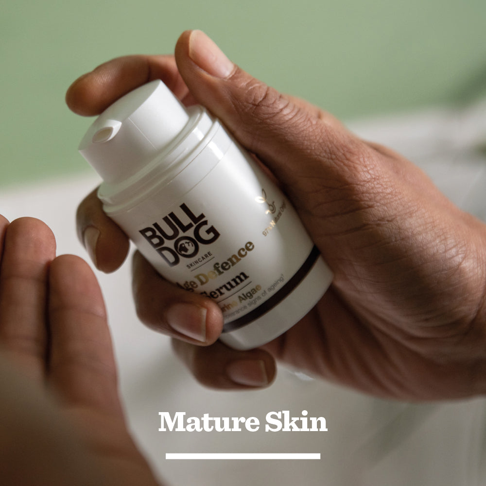 A person’s hands hold a bottle from the Age Defence Skincare Routine Bundle against a soft-focus background, with Mature Skin at the bottom—ideal for any skincare routine owing to its antioxidant complex.