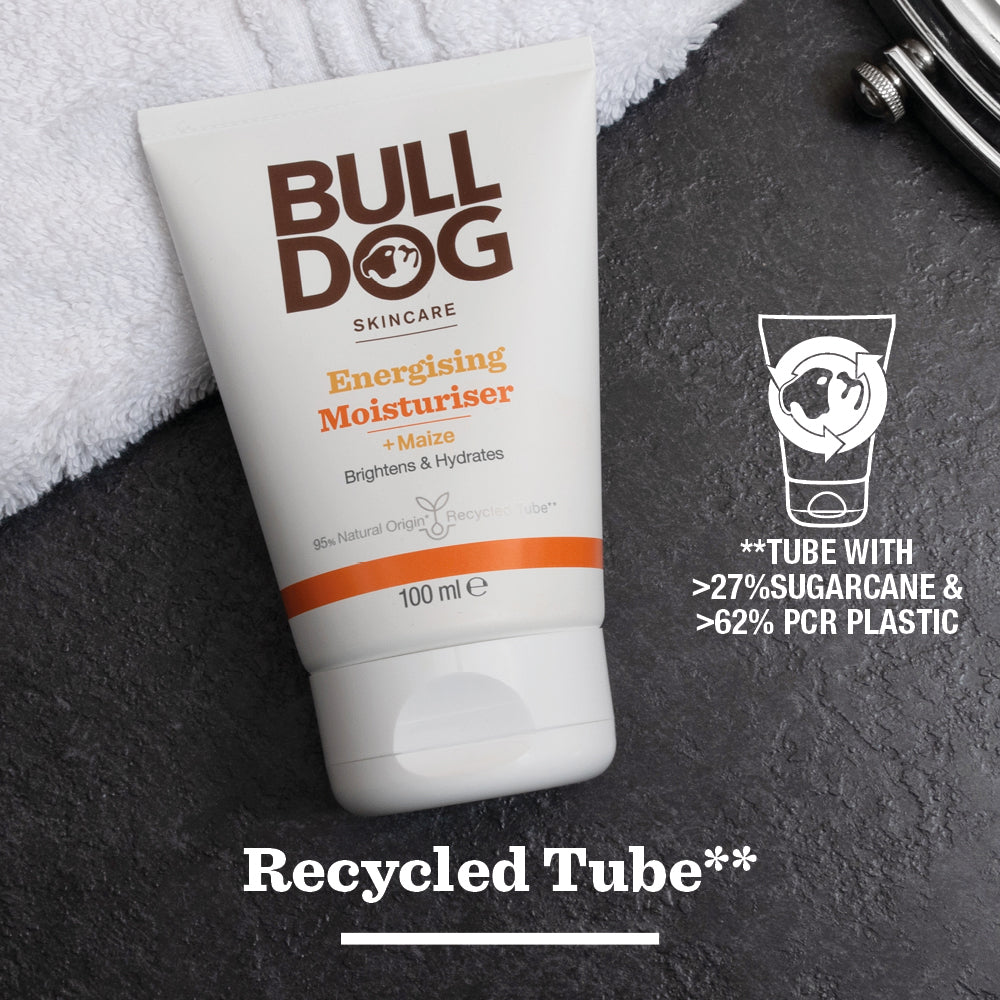 A white tube of Energising Moisturiser for men with maize sits on a dark surface. The text highlights its brightening properties and eco-friendly packaging with over 27% sugarcane and 62% PCR plastic.
