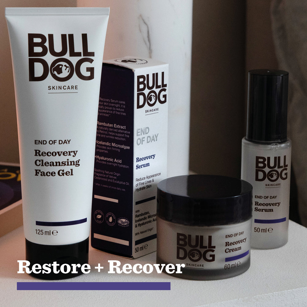 A set of Bulldog Skincare products, including the End of Day Recovery Cleansing Face Gel with Turmeric Extract, recovery serum, and recovery cream, arranged on a surface with a box and the words Restore + Recover below.