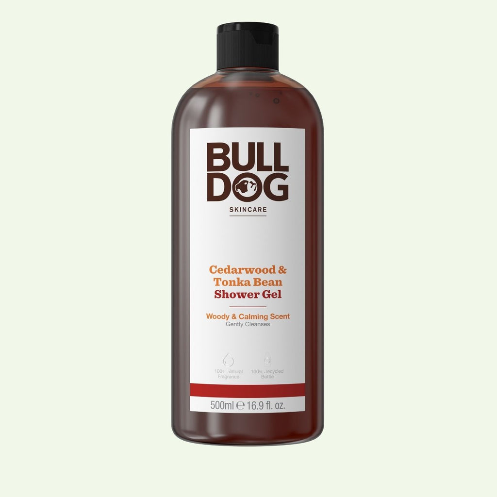 A 500ml bottle of Cedarwood & Tonka Bean Shower Gel with a black cap. The label highlights its calming, natural woody fragrance and notes it is gently cleansing.