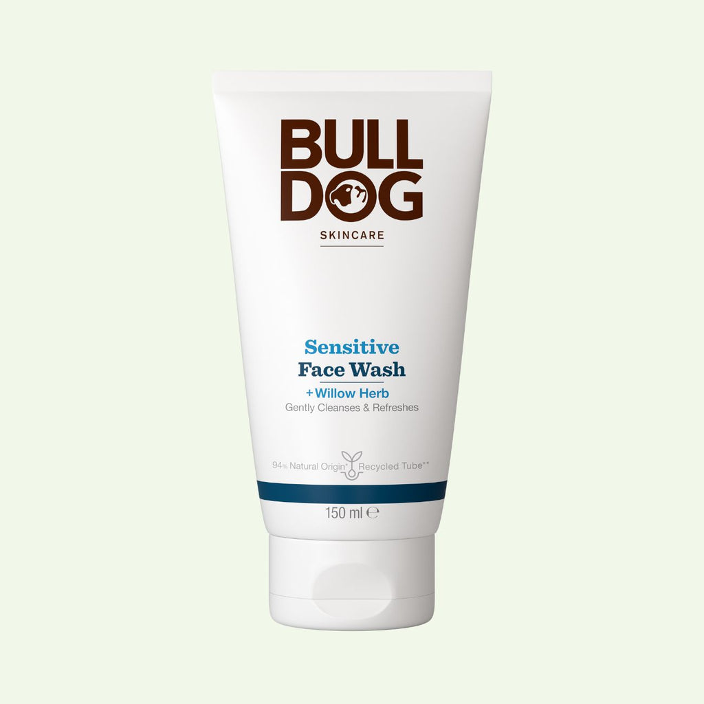 A 150 ml white tube of Sensitive Face Wash with willow herb and natural origin ingredients is shown on a light green background. The packaging displays brown and blue branding and product details.