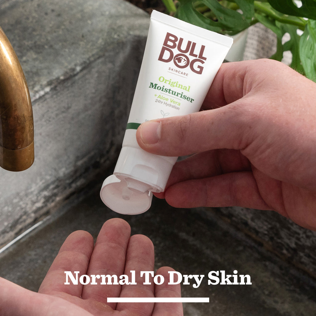 Someone squeezes a Bulldog Original Mini Skincare Trio moisturiser onto their hand by a sink, with "Normal To Dry Skin" text—ideal for men's skincare gift sets or as Bulldog gifts for men.