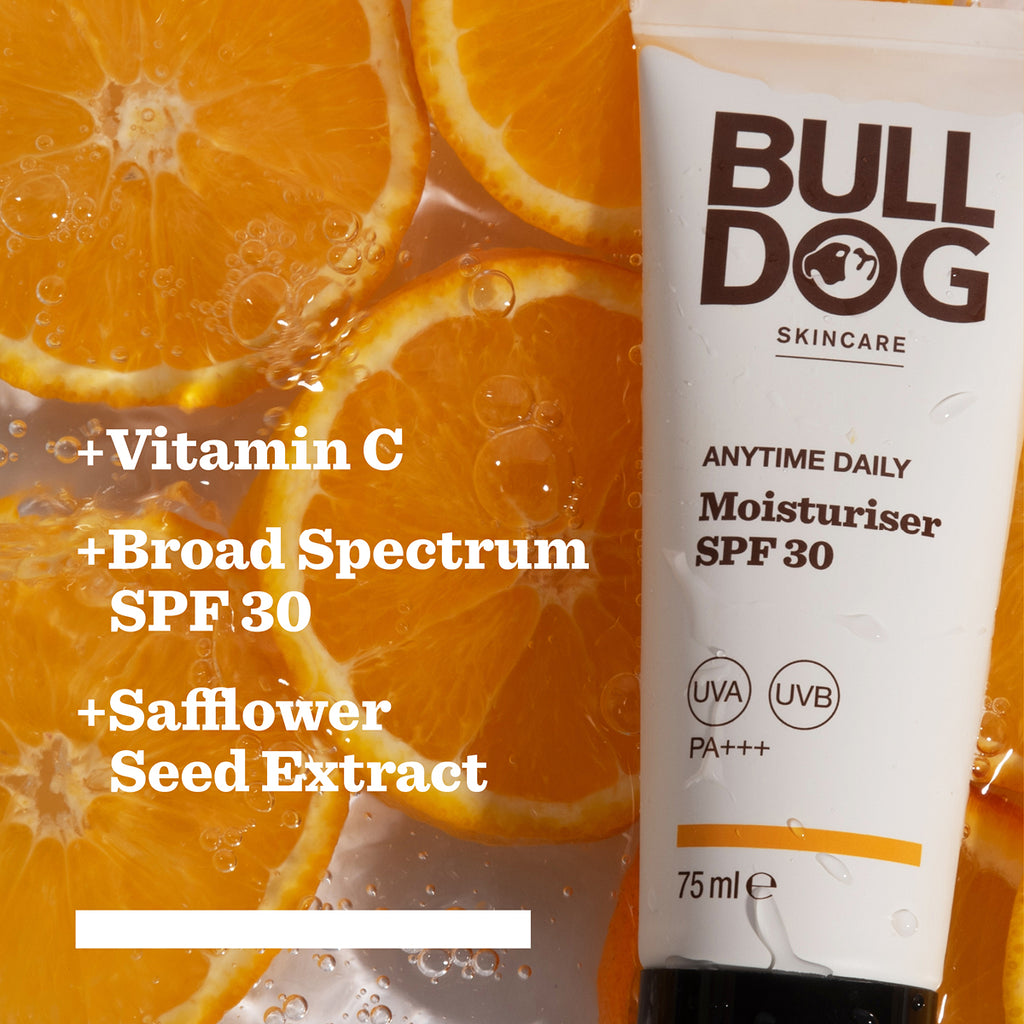 A tube from the Anytime Daily Collection Bundle lies on orange slices. Text highlights: Vitamin C, Broad Spectrum SPF 30, Safflower Seed Extract, and natural origin ingredients.