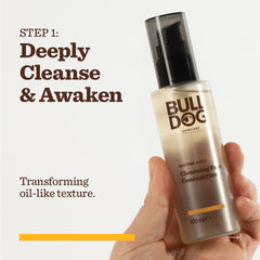 A hand holds a bottle from the Anytime Daily Collection Bundle. Text reads: STEP 1: Deeply Cleanse & Awaken. Features transforming oil-like texture, black pump, and clear packaging. Made with natural origin ingredients.